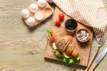Board with tasty croissant sandwich on wooden table�