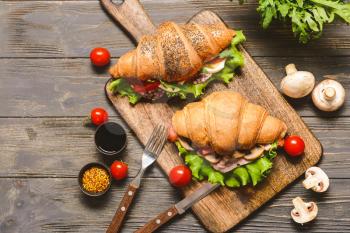 Board with tasty croissant sandwiches on wooden table�