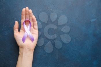 Female hand with lilac ribbon on color background. Cancer awareness concept�