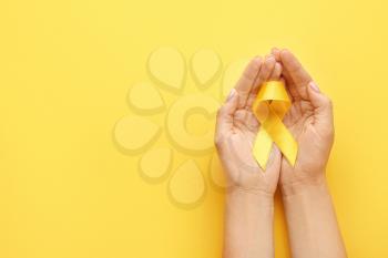 Female hands with yellow ribbon on color background. Cancer awareness concept�