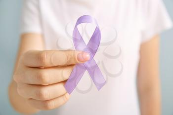 Young woman with lilac ribbon on grey background, closeup. Cancer awareness concept�