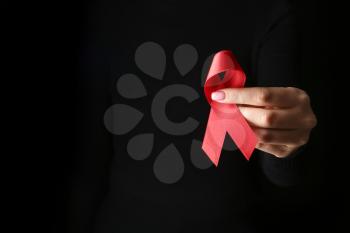 Female hand with red ribbon on dark background. AID awareness concept�