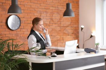 Young female receptionist talking by telephone at desk in hotel�