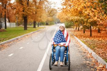 Handicapped young woman with USA flag in autumn park�
