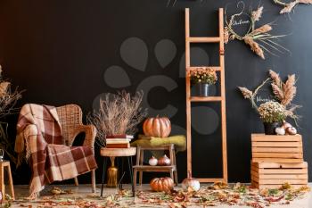 Beautiful autumn composition with wicker armchair near dark wall�