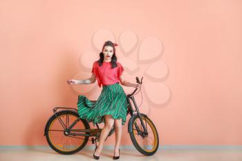 Portrait of beautiful tattooed pin-up woman with bicycle near color wall�