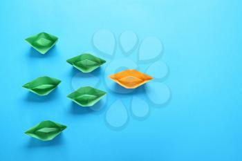 Orange origami boat among green ones on color background. Concept of uniqueness�