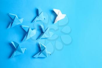 White origami bird among blue ones on color background. Concept of uniqueness�