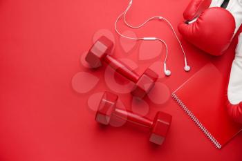 Dumbbells with boxing gloves, earphones and notebook on color background�