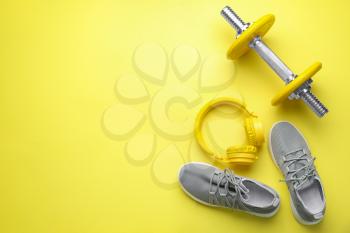 Dumbbell with shoes and headphones on color background�