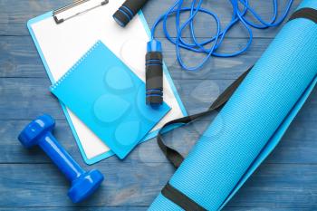 Dumbbell with notebook, clipboard, yoga mat and skipping rope on wooden background�