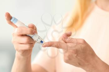 Diabetic woman taking blood sample with lancet pen at home, closeup�