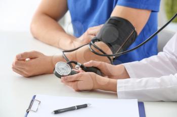 Doctor measuring blood pressure of young man in clinic�