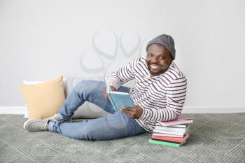 African-American man reading book near light wall�