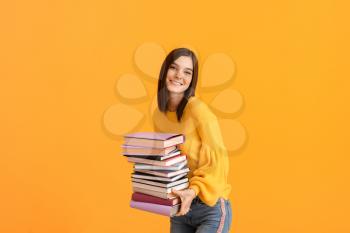 Beautiful young woman with many books on color background�