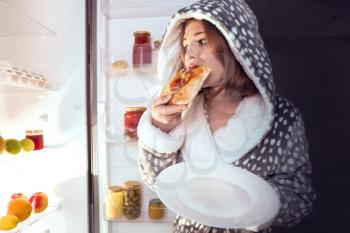 Teenage girl eating unhealthy food near refrigerator at night�