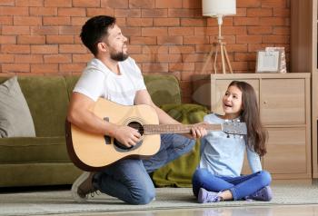 Little daughter and her father playing guitar at home�
