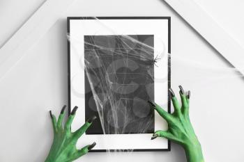 Hands of witch near photo frame indoors. Halloween celebration�