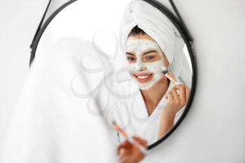Beautiful young woman applying facial mask in bathroom�