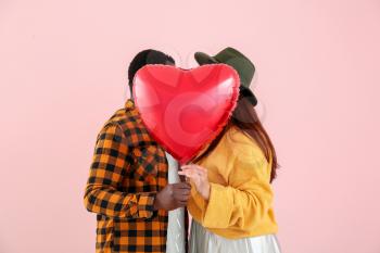 Happy interracial couple with heart-shaped balloon on color background�
