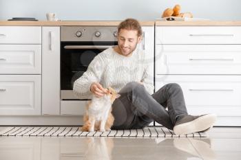 Man feeding cute cat in kitchen�