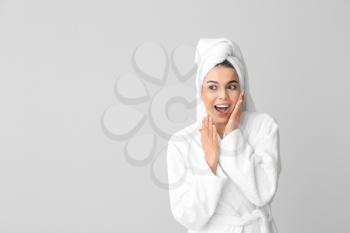 Surprised young woman in bathrobe on grey background�