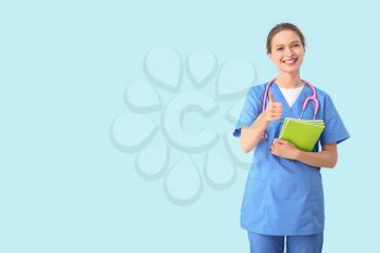 Female medical student showing thumb-up gesture on color background�