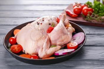 Frying pan with raw chicken and vegetables on wooden background�