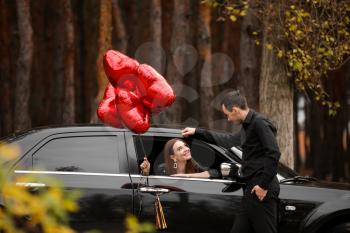 Man near his girlfriend with air balloons sitting in car. Valentine's Day celebration�