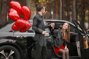 Man with air balloons helping his girlfriend to get out of car. Valentine's Day celebration�
