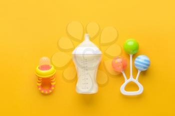 Bottle of milk for baby and toy with pacifier on color background�