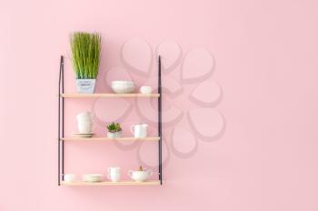 Shelves with tableware hanging on color wall�