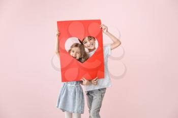Cute little children holding paper sheet with hole in shape of heart on color background. Valentines Day celebration�