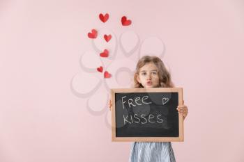 Cute little girl holding chalkboard with written text FREE KISSES on color background. Valentines Day celebration�