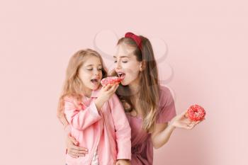 Cute mother and little daughter with tasty donuts on color background�