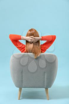 Beautiful woman relaxing in armchair against color background, back view�