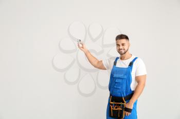 Male technician with air conditioner remote control on light background�