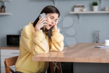 Worried young woman talking by phone at home�