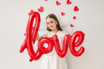 Beautiful young woman with balloon in shape of word LOVE and hearts on light background. Valentine's Day celebration�