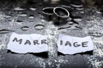 Torn paper with word MARRIAGE and rings on grunge background. Concept of divorce�