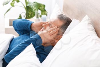 Mature man suffering from head ache while lying in bed�