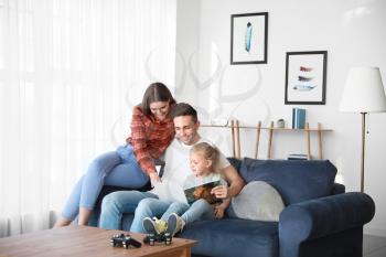 Happy young family reading book while sitting on sofa at home�