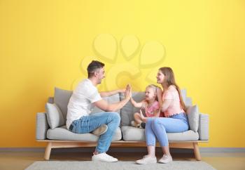 Happy young family playing while sitting on sofa near color wall�