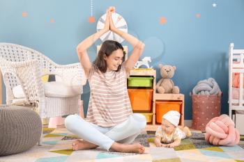 Young mother with little baby meditating at home�