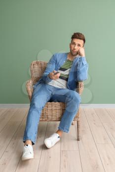 Bored man watching TV while sitting in armchair near color wall�