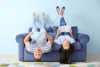 Young couple reading books while lying on sofa at home�