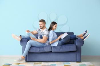 Young couple reading books while sitting on sofa at home�