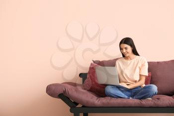 Young woman with laptop sitting on sofa at home�