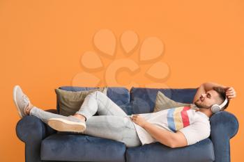 Young man listening to music while lying on sofa at home�