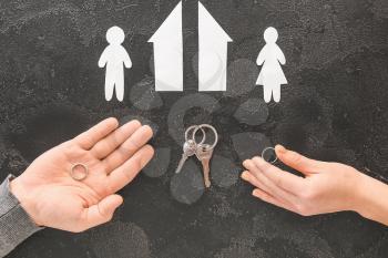 Male and female hands with wedding rings, keys, cut figures of house and couple on dark background. Concept of divorce�